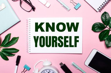 SENİN, iş aksesuarları ve yeşil yapraklarla çevrili pembe bir arka plan üzerine beyaz bir deftere yazıldığını biliyorsun..