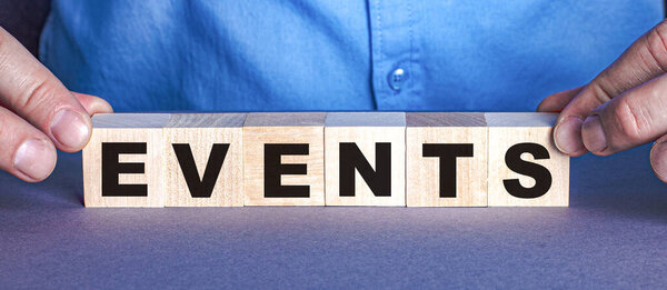 The word EVENTS is made up of wooden cubes by a man. Business concept