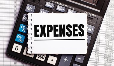 Masanın üzerinde raporlar, bir hesap makinesi ve üzerinde ExpENSES yazan bir kart var. İş konsepti