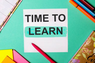 Parlak çıkartmalar, not defterleri ve kalemlerin yanında turkuaz bir arkaplanda yazanları öğrenme zamanı.