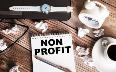 Tahta bir masanın üzerinde bir fincan kahve, bir saat, bardaklar ve üzerinde NON PROFIT yazan bir defter var. İş konsepti