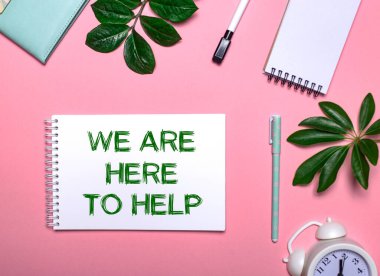 Biz yardım etmek için buradayız. Yeşil bir not defterine yeşil bir not defteri ile yazılmıştır. Pembe arka planda, not defterleri, kalemler, beyaz çalar saat ve yeşil yapraklarla çevrili. Eğitici kavram