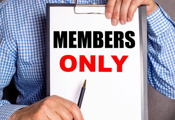 The man points with a pen to the phrase MEMBERS ONLY on a white sheet.