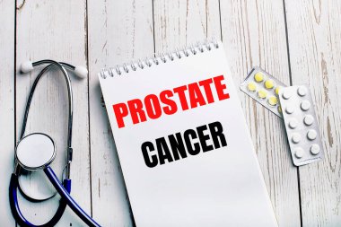 Hafif ahşap bir masada steteskop, haplar ve içinde Prostate CanCER yazan bir defter bulunur. Tıbbi konsept