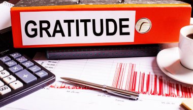 Kırmızı belge klasöründe kahve, hesap makinesi ve kalemin yanında GRATITUDE yazıyor..
