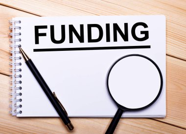 Hafif, ahşap bir arka planda bir kalem, bir büyüteç ve üzerinde 