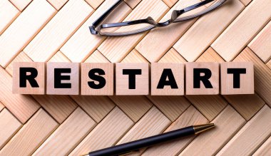 RESTART kelimesi tahta bir arka planda, bir kalem ve gözlüğün yanındaki tahta küplere yazılmıştır..