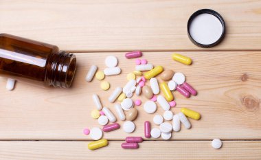 Ahşap arka planda çok renkli haplarla açılmış bir ilaç şişesi. Tıbbi konsept. Eczacılık.