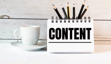 CONTENT kelimesi beyaz bir not defterine beyaz bir fincanın yanında hafif bir arka planda yazılır.