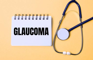 Bej bir arka planda, steteskop ve GLAUCOMA yazılı beyaz bir not defteri. Tıbbi konsept