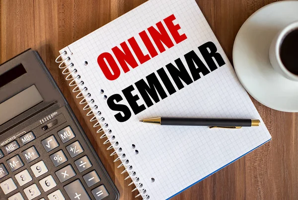 ONLINE SEMINAR written in a white notepad near a calculator and a cup of coffee on a dark wooden background