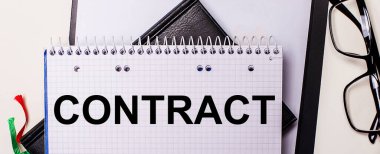 ConTRACT siyah çerçeveli gözlüklerin yanındaki beyaz bir deftere kırmızı ile yazılmıştır..