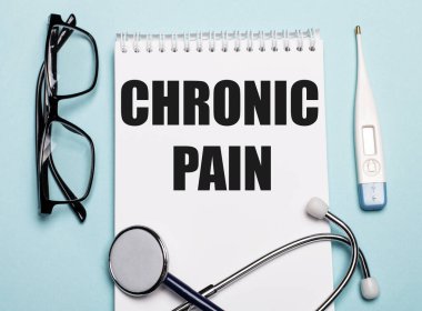Beyaz bir not defterine steteskop, gözlük ve açık mavi arka planda elektronik termometre ile yazılmış CHRONIC PaIN. Tıbbi konsept.