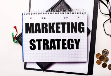Hafif bir arka plan gözlüğü, bozuk paralar ve üzerinde MarkeTing STRATEGY yazan bir defter. İş konsepti