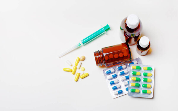 Multicolored pills, syringe and medical bottles on a light background. Medical concept