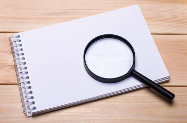 Boş not defteri ve hafif ahşap arka planda büyüteç. Boşluğu kopyala
