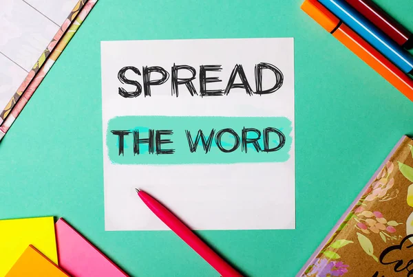 SPREAD THE WORD written on a turquoise background near bright stickers, notepads and markers