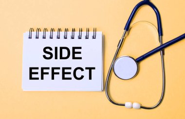 Bej bir arka planda, steteskop ve üzerinde yazı olan beyaz bir not defteri var. Tıbbi konsept