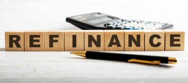 REFINANCE kelimesi bir hesap makinesi ve bir kalem arasındaki tahta küplere yazılmıştır. İş konsepti.