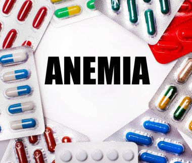 ANEMIA, içinde haplar olan çok renkli paketlerle çevrili açık bir arkaplanda yazılıdır. Tıbbi konsept