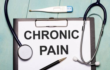 Açık mavi ahşap arka planda CHRONIC PaIN, stetoskop, elektronik termometre ve kalem etiketli bir kağıt var. Tıbbi konsept