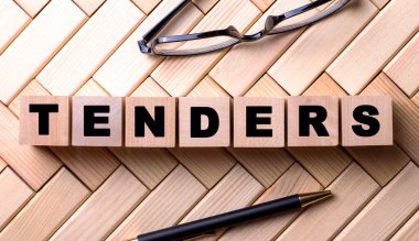 TENDERS kelimesi tahta bir arka planda, bir kalem ve gözlüğün yanındaki tahta küplere yazılmıştır..