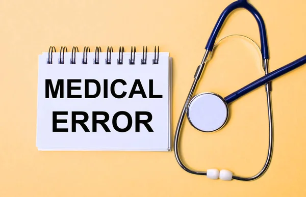 On a beige background, a stethoscope and a white notepad with the inscription MEDICAL ERROR. Medical concept