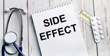 Hafif ahşap bir masada steteskop, haplar ve üzerinde yazı olan bir defter bulunur. Tıbbi konsept