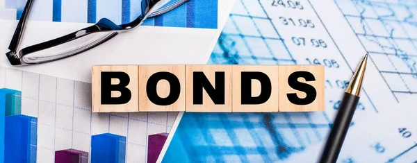 Parlak diyagramlarda, gözlüklerde, bir kalem ve tahtadan küplerde BONDS yazıyor. İş konsepti