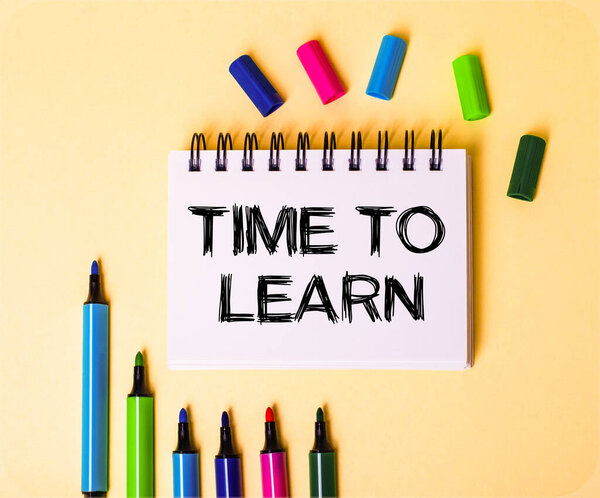 TIME TO LEARN написана в белой тетради на бежевом фоне рядом с разноцветными маркерами