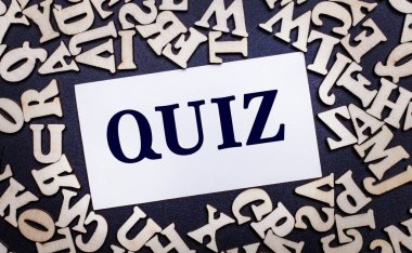 Hafif bir arkaplanda İngiliz alfabesinin ahşap harfleri ve içinde QUIZ yazan beyaz bir kart var.