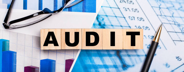 On the bright diagrams, glasses, a pen and wooden cubes with the word AUDIT. Business concept