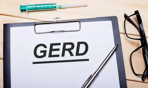 GERD kelimesi siyah çerçeveli gözlük, kalem ve şırınganın yanındaki beyaz bir kağıt parçasına yazılmıştır. Tıbbi konsept
