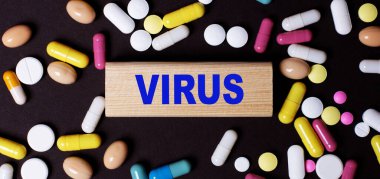 Karanlık bir arka planda, çok renkli haplar ve tahta bir blokta VIRUS kelimesi. Tıbbi konsept