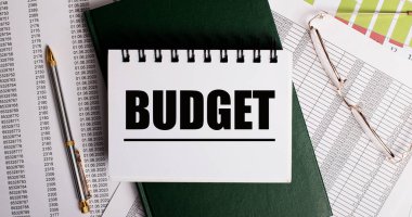 Masaüstünde raporlar, gözlükler, bir kalem, yeşil bir günlük ve üzerinde 