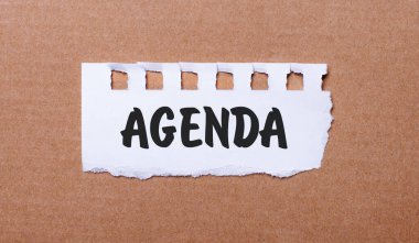 Kahverengi arka planda, üzerinde AGENDA yazılı beyaz kağıt