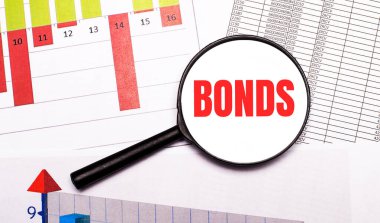 Masaüstünde, grafikler, raporlar, üzerinde BONDS yazan bir büyüteç. İş konsepti
