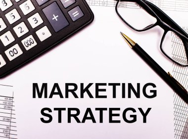 Raporlarda bir hesap makinesi, bir gözlük, bir kalem ve üzerinde MARKETING STRATEGY yazan bir defter var.