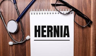 HERNIA kelimesi, steteskop ve siyah çerçeveli gözlüklerin yanındaki tahta bir arka planda beyaz kağıda yazılmıştır. Tıbbi konsept