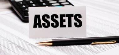 Masanın üzerinde raporlar, bir kalem, bir hesap makinesi ve ASSETS yazılı bir beyaz kart var. Odaklanmayın