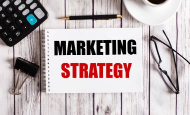 MARKETING STRATEGY bir hesap makinesi, kahve, bardak ve bir kalem yakınındaki beyaz bir not defterine yazılmıştır. İş konsepti