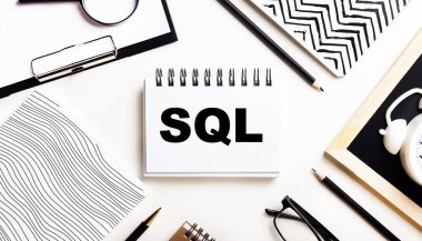 Bir ışık masasında defterler, bir büyüteç, bir çalar saat, bir gözlük ve bir kalem vardır. Ortasında da SQL yazılı bir defter var.