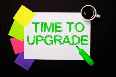 Üzerinde Time to UPGRADE yazan bir sayfa kağıt, bir fincan kahve, notlar için parlak renkli çıkartmalar ve siyah arka planda yeşil bir kalem. Yukarıdan görüntüle.