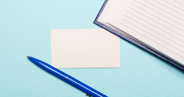 Notitieblok, witte pen en blanco kaart voor het invoegen van tekst of illustraties op een lichtblauwe achtergrond. Bovenaanzicht met kopieerruimte — Stockfoto