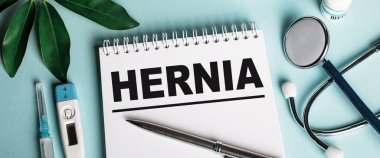 Mavi bir arka planda beyaz bir defterde, bir deri değiştirici, bir stetoskop, bir şırınga ve bir elektronik termometre yakınında, HerNIA kelimesi yazılır. Tıbbi konsept