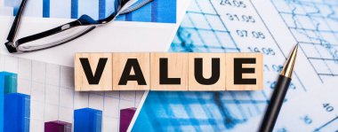 Parlak diyagramlarda, gözlüklerde, bir kalem ve VALUE yazan tahta küplerde. İş konsepti