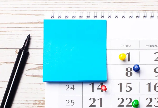 En una mesa de madera clara hay un calendario, una pegatina azul con un lugar para insertar texto y un marcador negro. Vista superior con espacio de copia — Foto de Stock