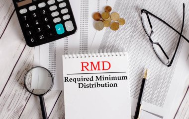 Hesap makinesinin yanındaki beyaz bir not defterine RMD yazılmış. Nakit, gözlük, büyüteç ve kalem. İş konsepti