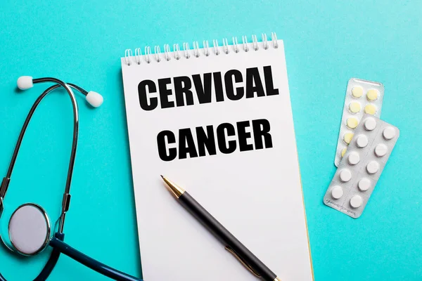 CERVICAL CANCER written in a white notepad near a stethoscope, pens and pills on a light blue background. Medical concept