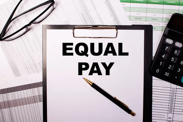 EQUAL PAY is written on a white sheet of paper, near the glasses and the calculator.